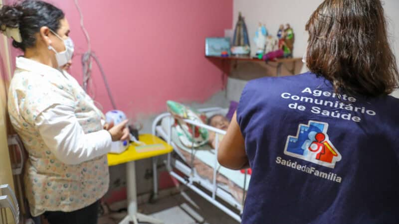Processo seletivo Belo Vale 2026 — agente comunitária de saúde em visita domiciliar ilustrativa